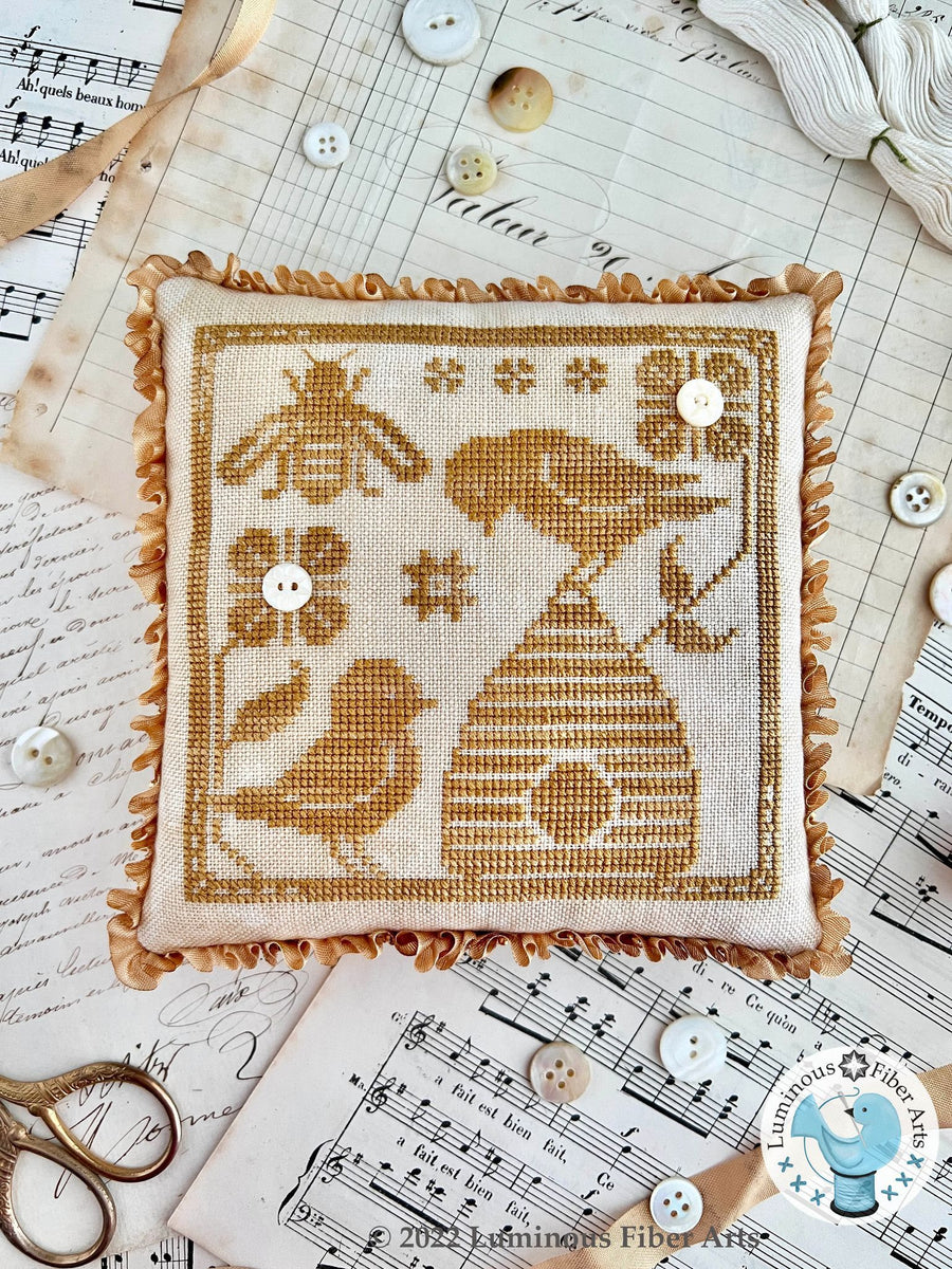 Embroidered square with bees and a beehive on a surface with buttons and thread
