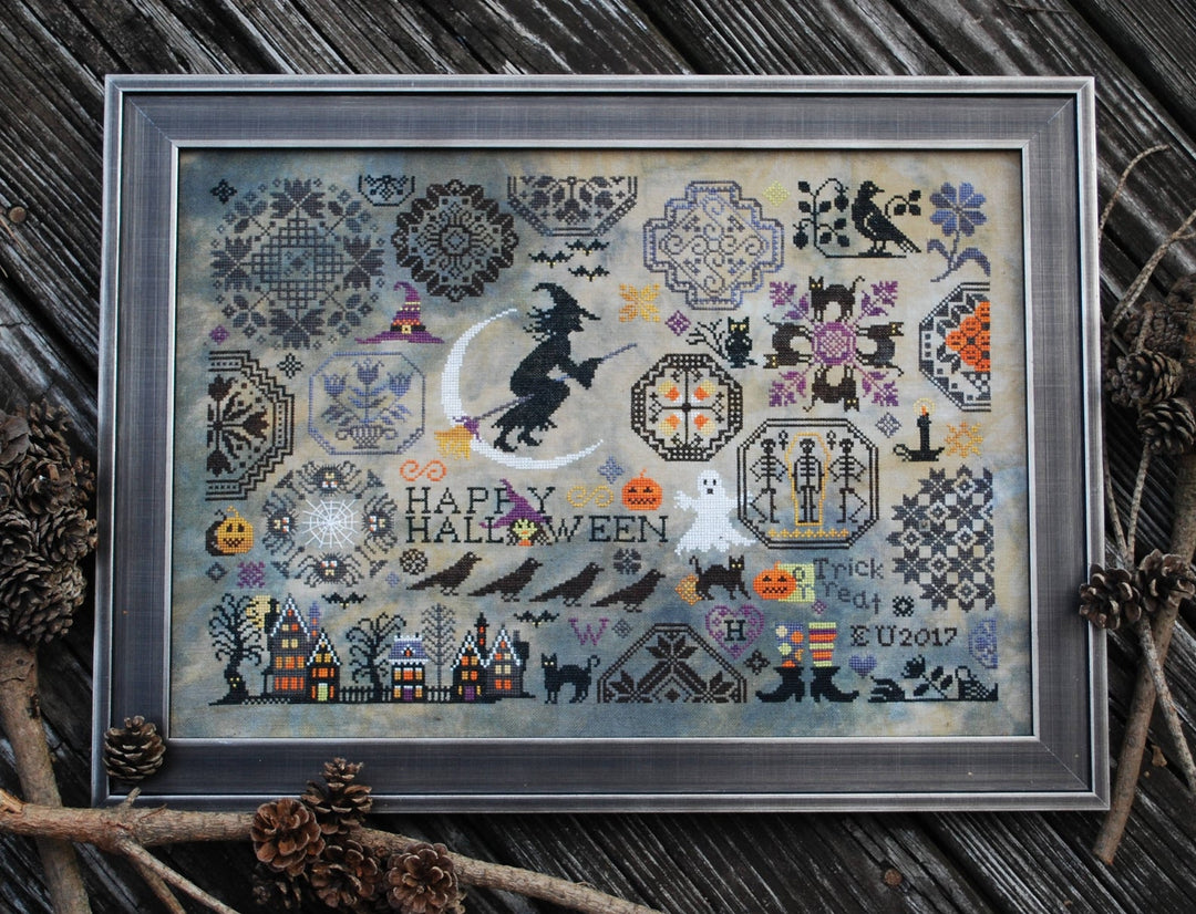 A framed cross-stitch kit depicting various Halloween-themed designs, including pumpkins, ghosts, and cats, with a 'Happy Halloween' message.