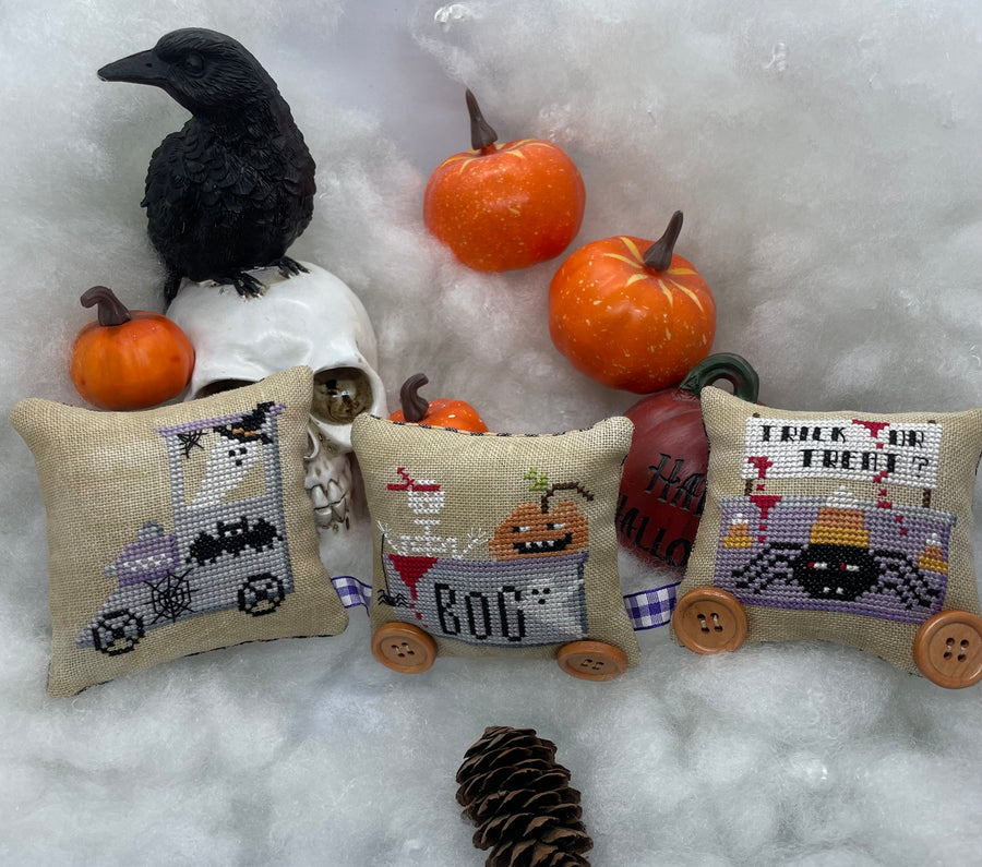 Decorative pillows with Halloween-themed designs on a snowy background with pumpkins and a crow.