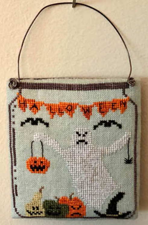 Halloween-themed cross-stitched design with a ghost, pumpkins, and decorative elements on a light blue background.
