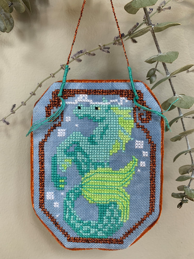 Cross-stitched dragon design on fabric with green leaves in the background
