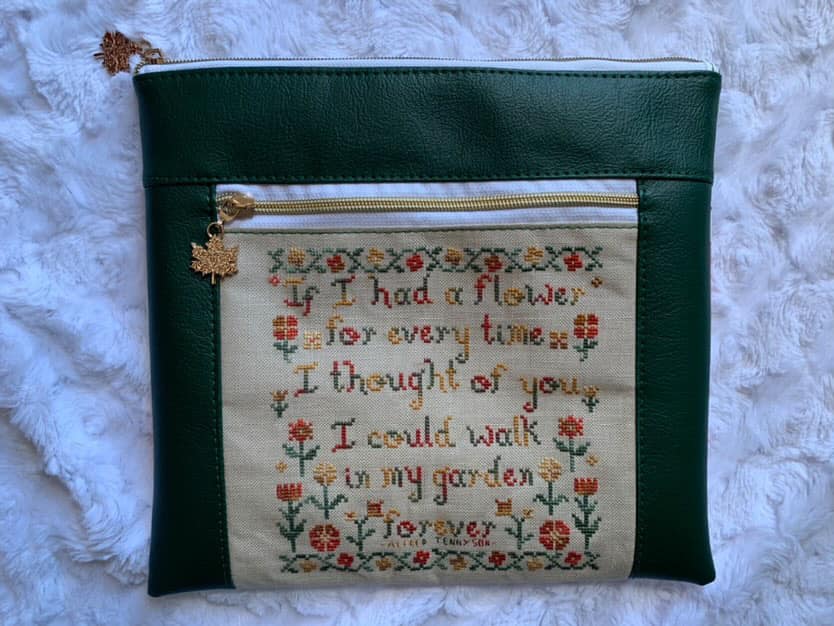 Green pouch with embroidered text and floral patterns on a textured white surface