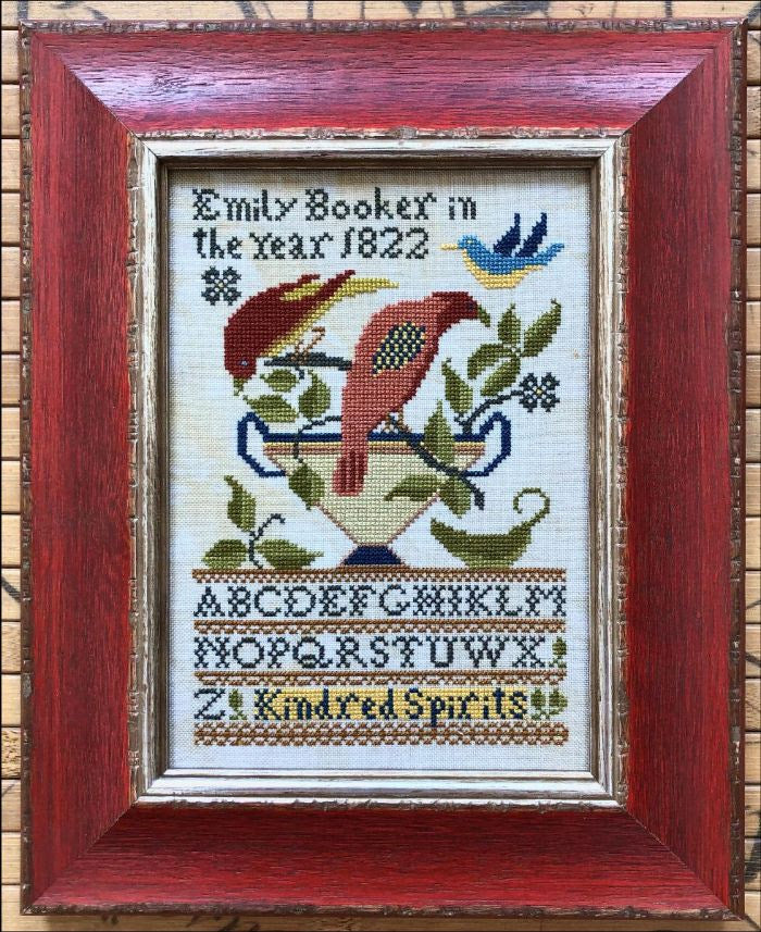 Framed cross-stitched piece with a bird design and text on a woven background