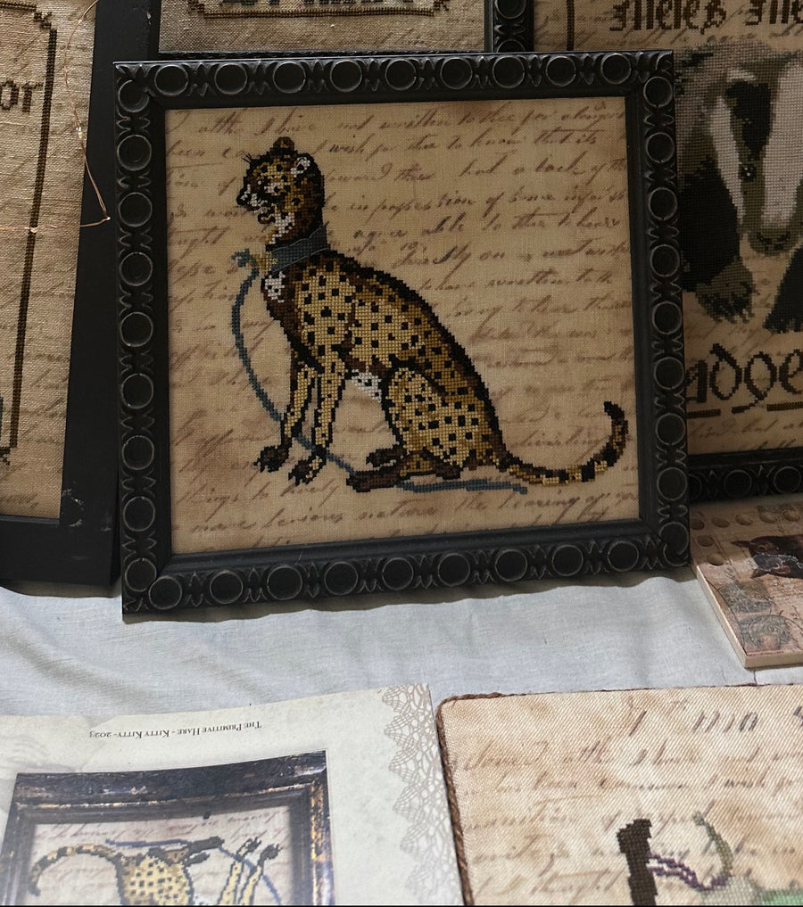 Framed cross-stitched picture of a cheetah on an old document background