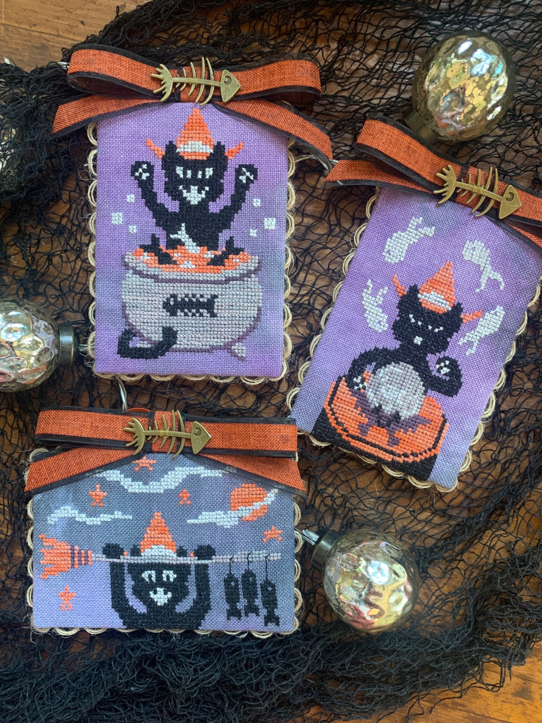Three Halloween-themed cross-stitched pieces on a dark background with decorative elements.