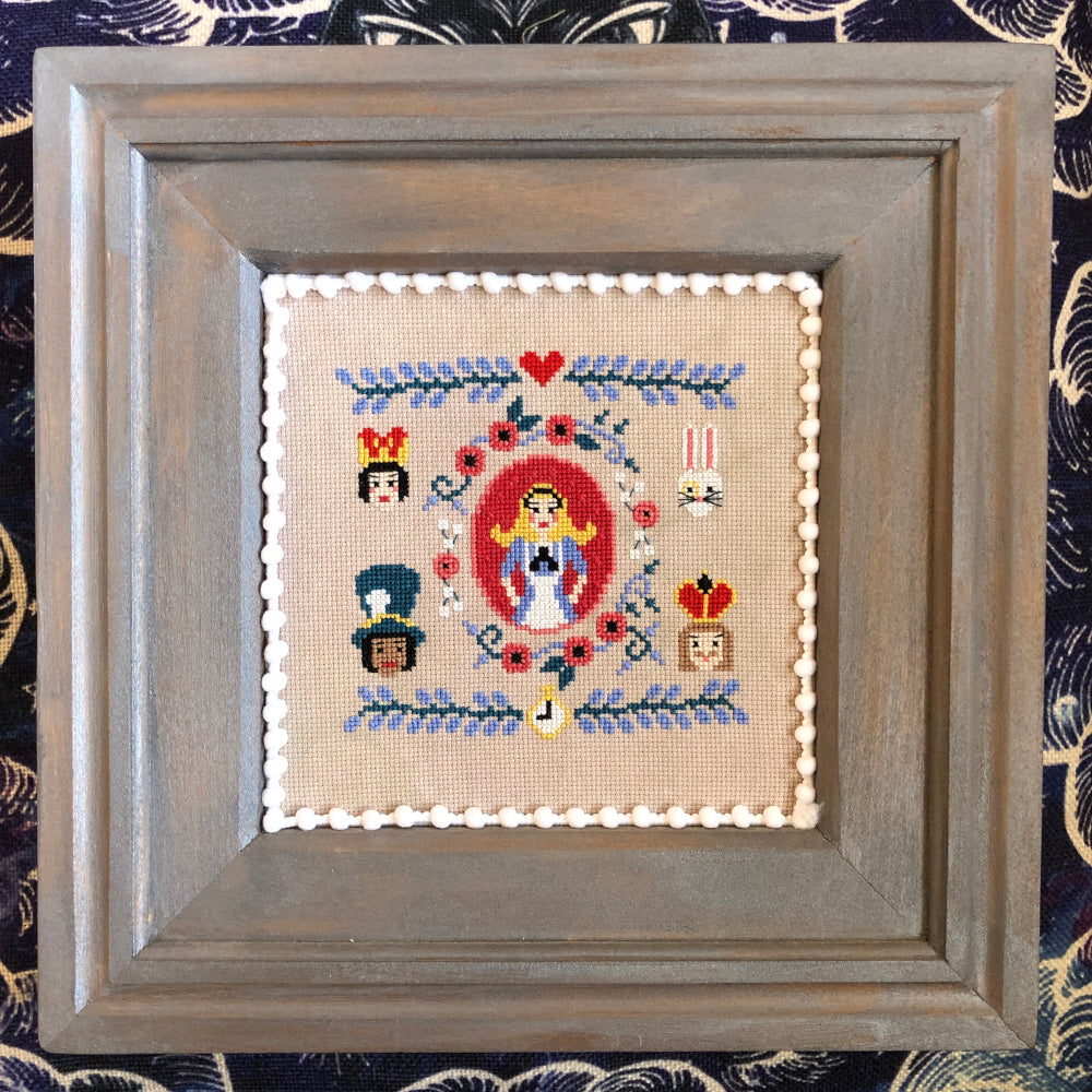 Framed cross-stitched piece with decorative elements on a patterned fabric background