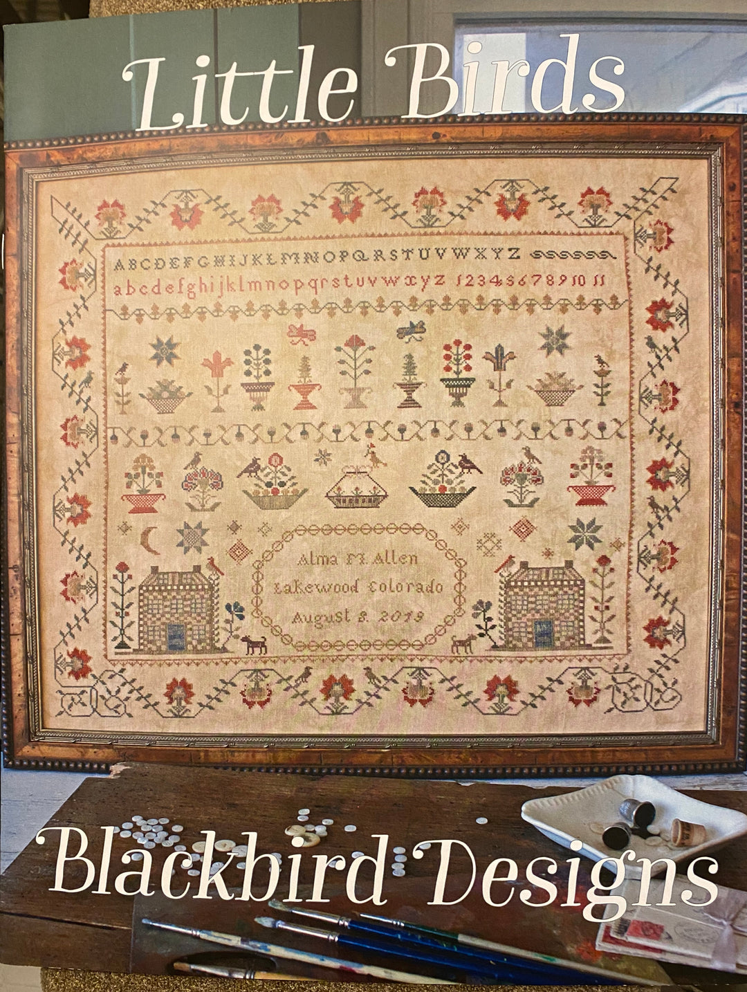 A completed needlepoint artwork titled 'Little Birds' featuring various birds and floral patterns, framed in a wooden frame.