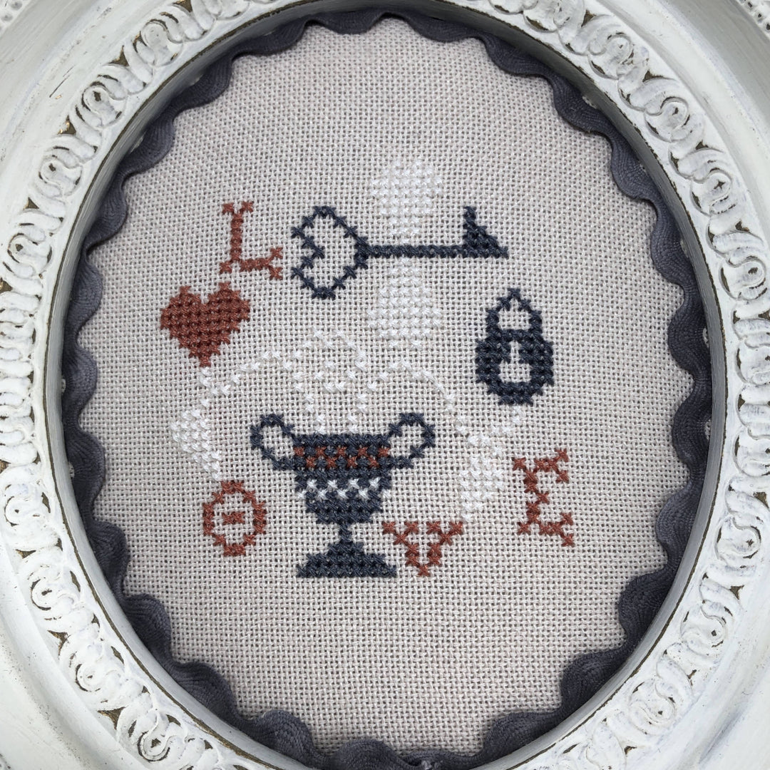 A cross-stitch chart with a Valentine's theme, featuring various embroidered designs including hearts and keys mainly in red, white, and gray colors on a beige background.
