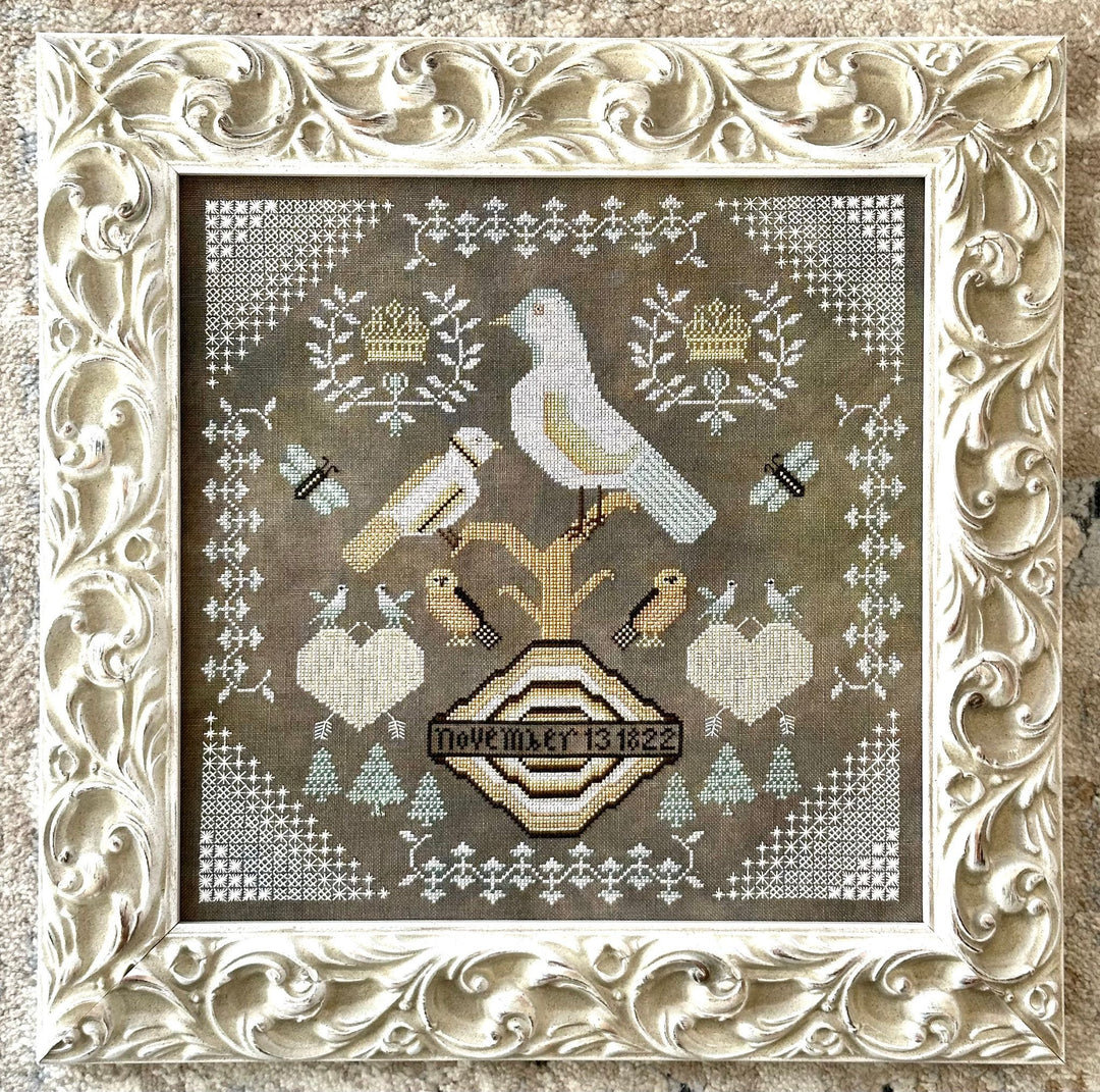 Decorative cross-stitched design with birds and geometric patterns in a ornate frame.