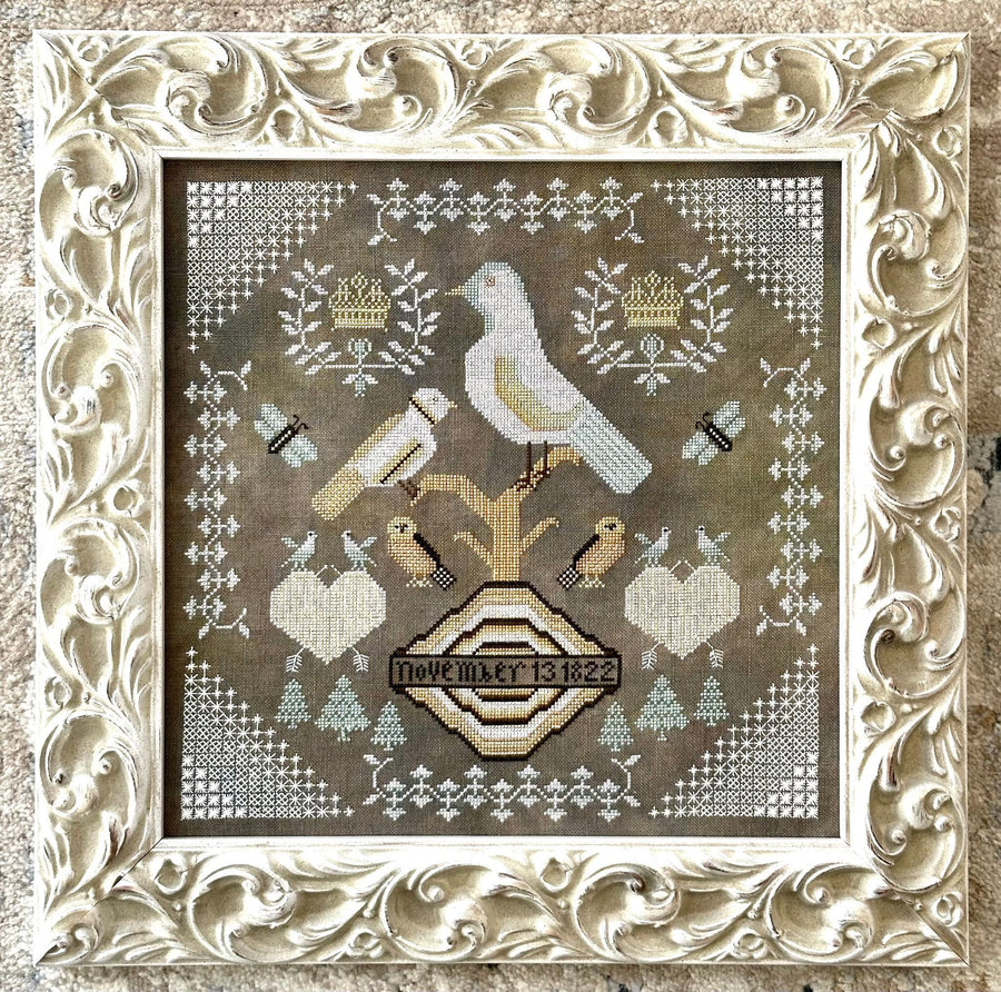 Decorative cross-stitched design with birds and geometric patterns in a ornate frame.