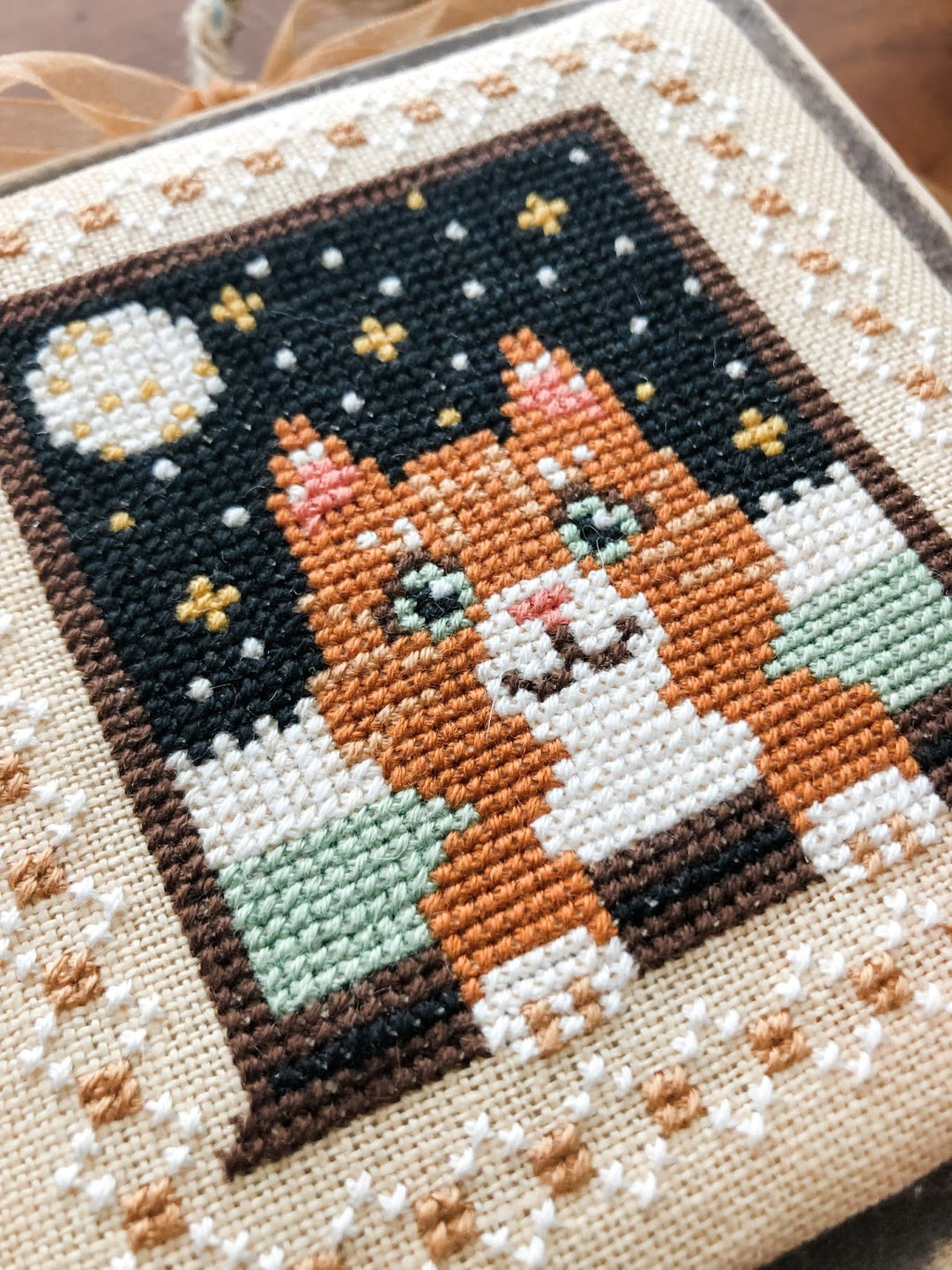 Cross-stitched picture of an orange cat with a moon and stars on fabric.
