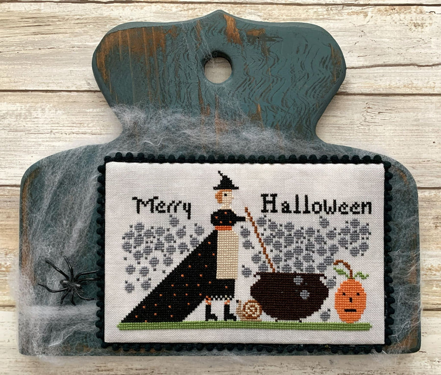 Decorative Halloween cutting board with cross-stitched design of a witch and text on a wooden background.