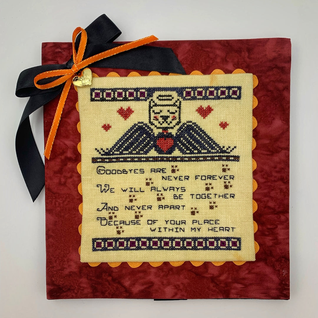A stitched memorial piece featuring a cat and dog design with a textual quote in the center, on a red background with an orange ribbon at the top.