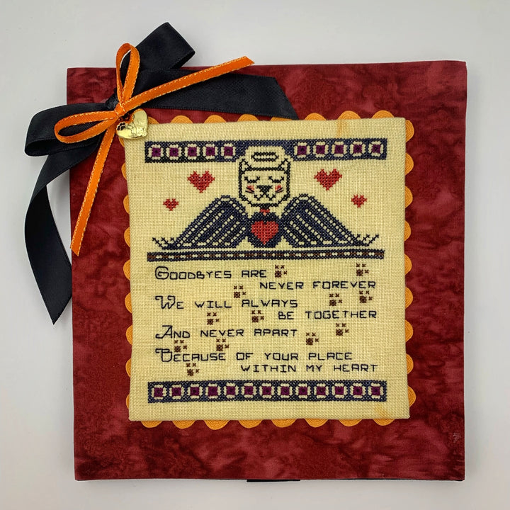 A stitched memorial piece featuring a cat and dog design with a textual quote in the center, on a red background with an orange ribbon at the top.