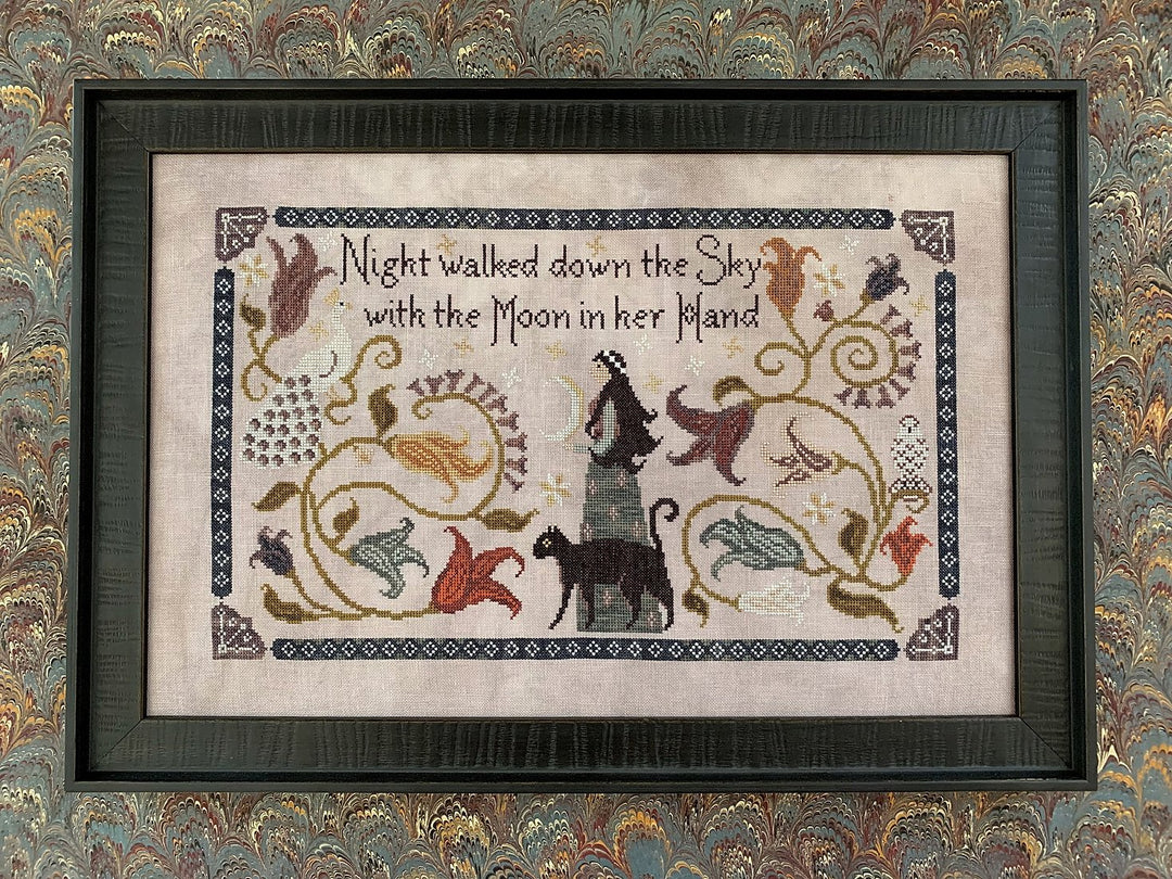 Cross-stitch needlework depicting a moonlit night scene with text, animals, and floral elements on a purple/gray linen background, framed.