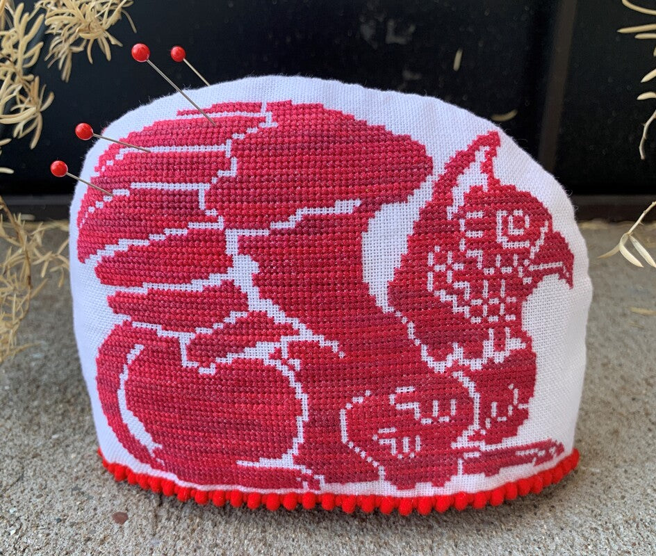 Cross-stitched cushion with red and white design on a textured surface