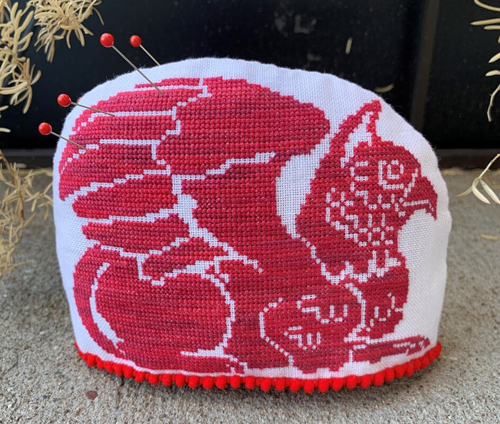 Cross-stitched cushion with red and white design on a textured surface