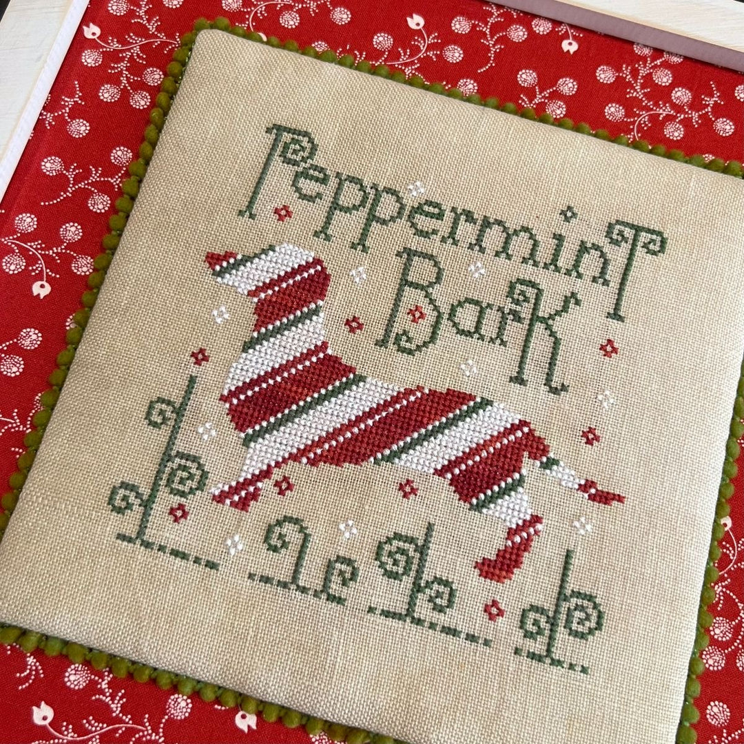 Cross-stitched design of a dog in a Santa hat with 'Peppermint Bark' text on beige fabric.