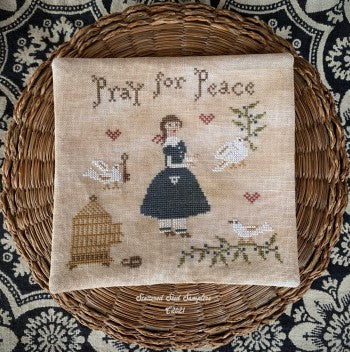 Cross-stitched fabric with 'Pray for Peace' text and design on a woven mat.
