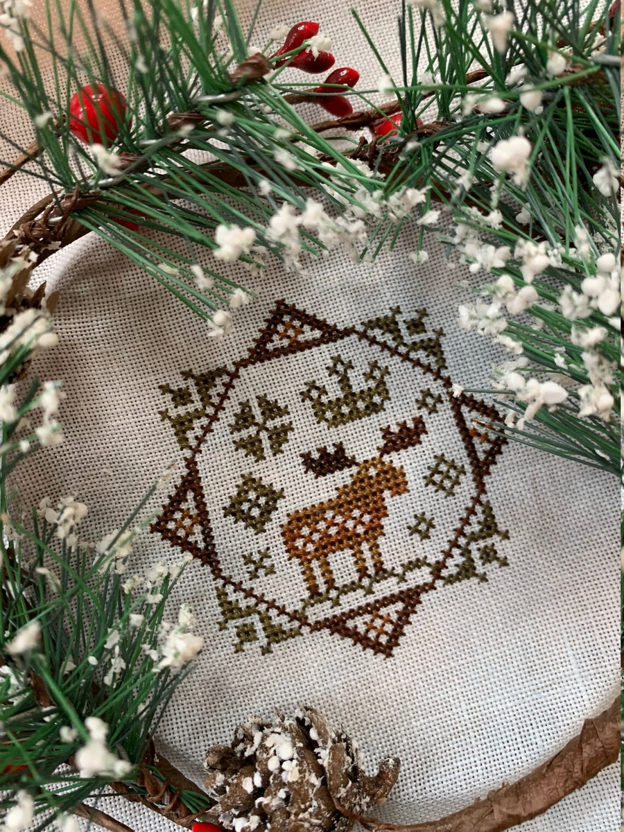 Embroidered design of a deer in a snowy landscape surrounded by greenery and berries.
