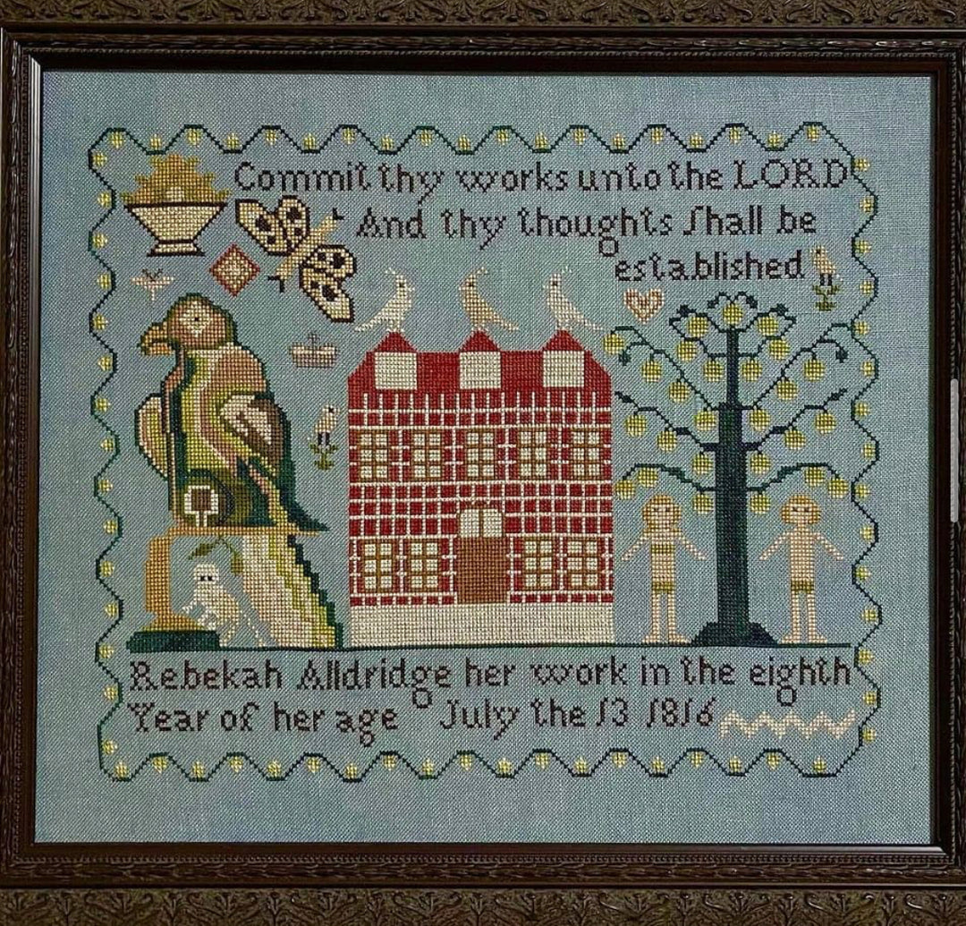 Embroidered sampler with text and decorative elements on a blue background