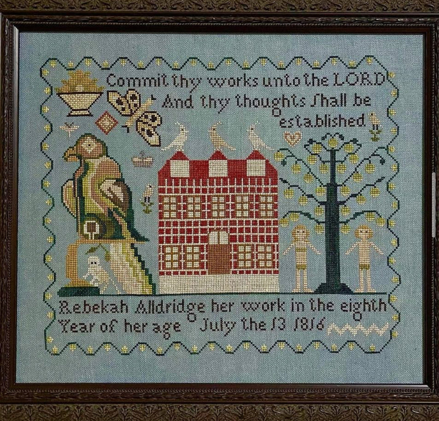 Embroidered sampler with text and decorative elements on a blue background