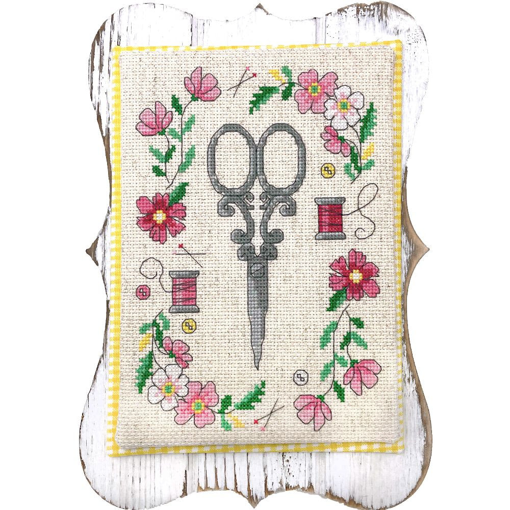 Cross-stitched design with scissors and flowers on a white background