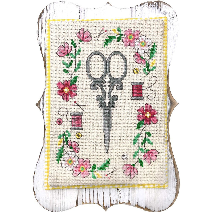 Cross-stitched design with scissors and flowers on a white background