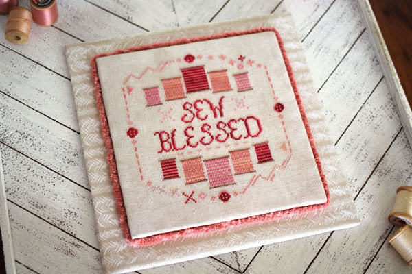 Embroidered pillow with 'Sew Blessed' text on a wooden surface