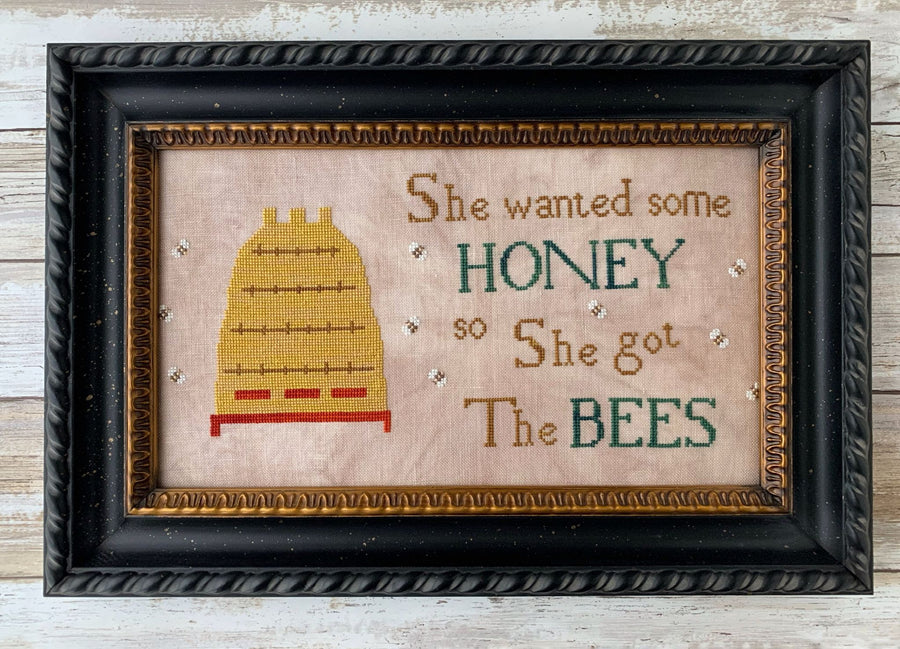 Framed cross-stitched picture with a bee and text on a wooden background