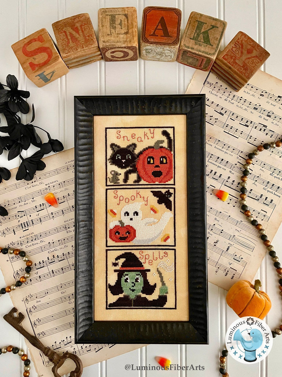 Framed Halloween-themed cross-stitch art on sheet music with decorative elements.