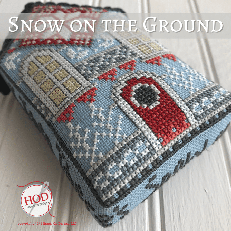 Cross-stitched blanket with winter scene design on a wooden surface, featuring the brand 'HOD' in the corner.
