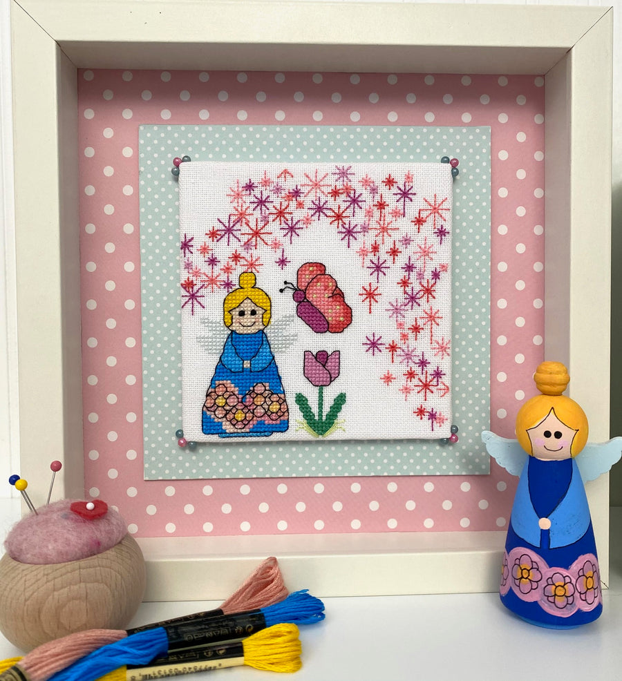 Framed cross-stitched picture of a fairy with a polka dot background, surrounded by sewing tools.