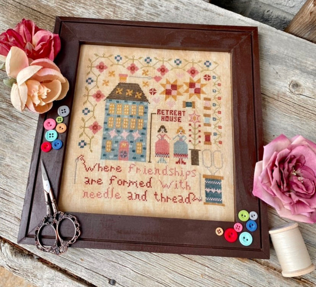 Framed cross-stitched artwork with decorative elements on a wooden surface
