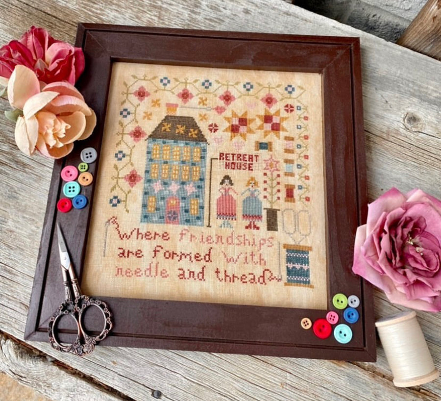 Framed cross-stitched artwork with decorative elements on a wooden surface