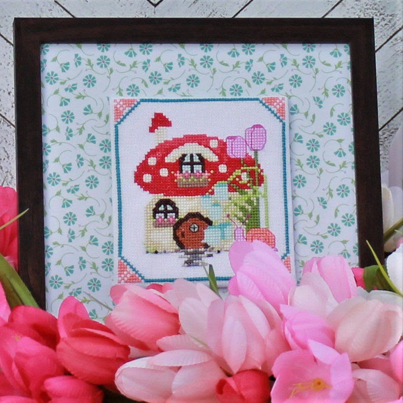 Framed cross-stitched picture of a mushroom with flowers in the foreground