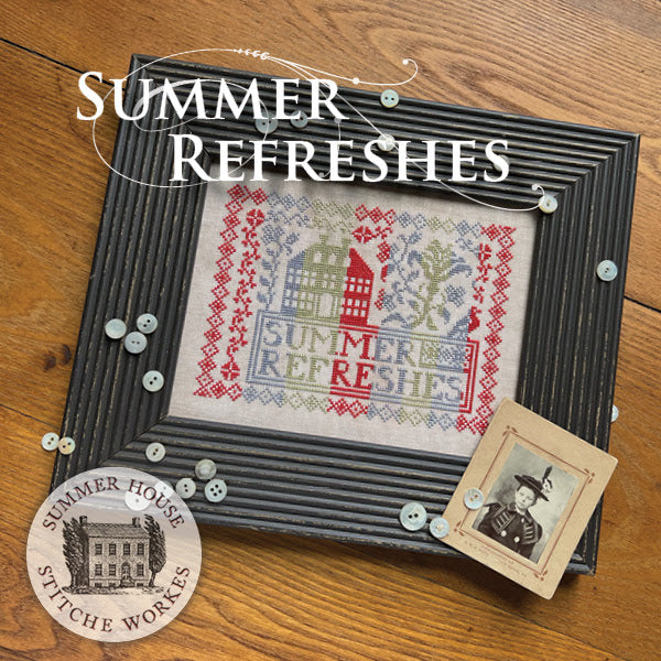 Framed cross-stitched piece with 'Summer Refreshes' text on a wooden surface, featuring decorative elements and branding.