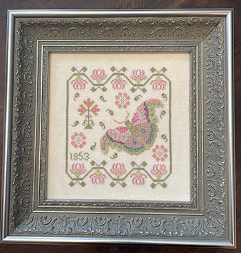 Framed cross-stitched butterfly with floral patterns on beige fabric.