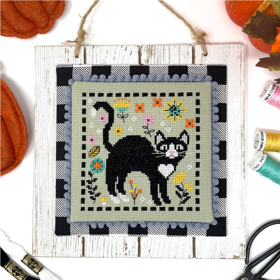 Embroidery hoop with a black cat design surrounded by autumn-themed decorations.