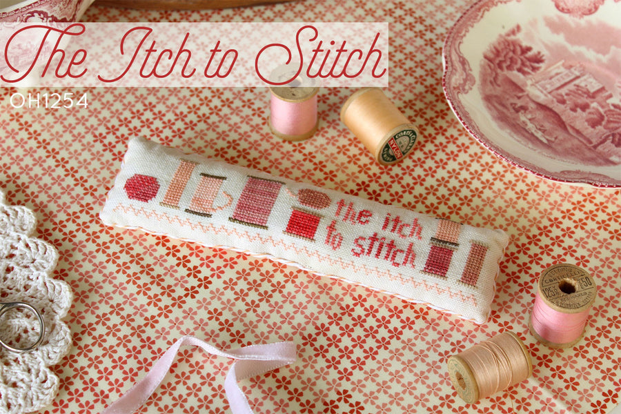 Cross-stitched pillow with 'the itch to stitch' text on a red floral fabric background.