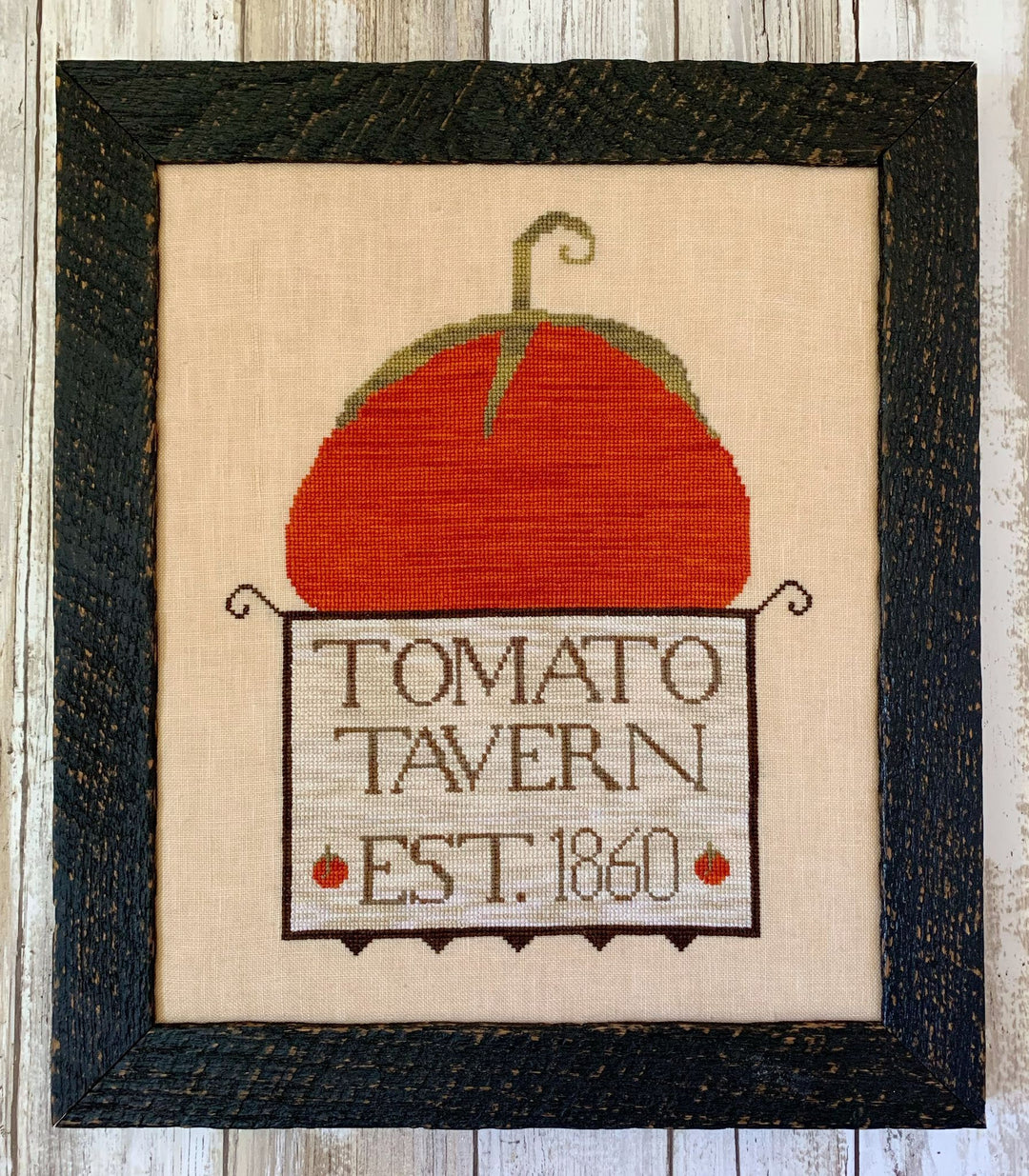Framed cross-stitched tomato with 'Tomato Tavern Est. 1860' text on a wooden background