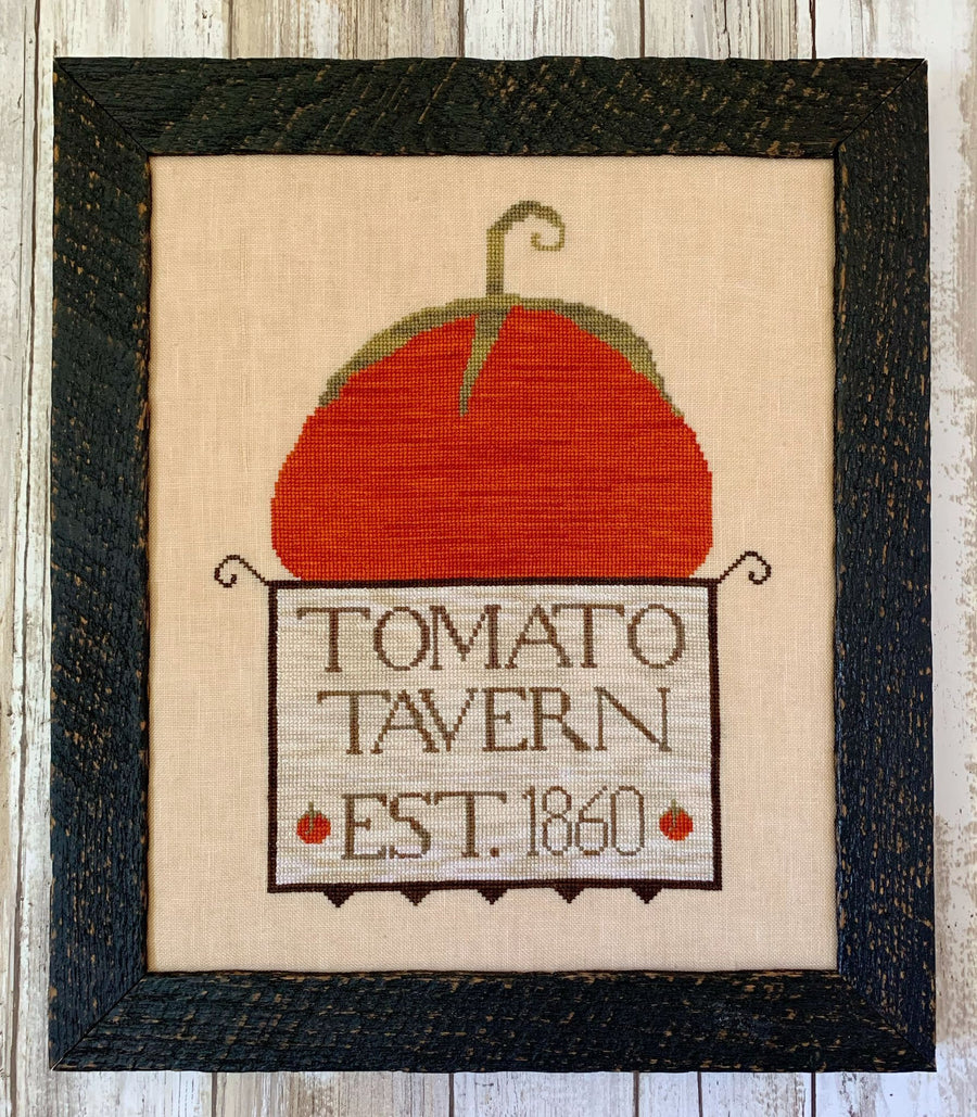 Framed cross-stitched tomato with 'Tomato Tavern Est. 1860' text on a wooden background