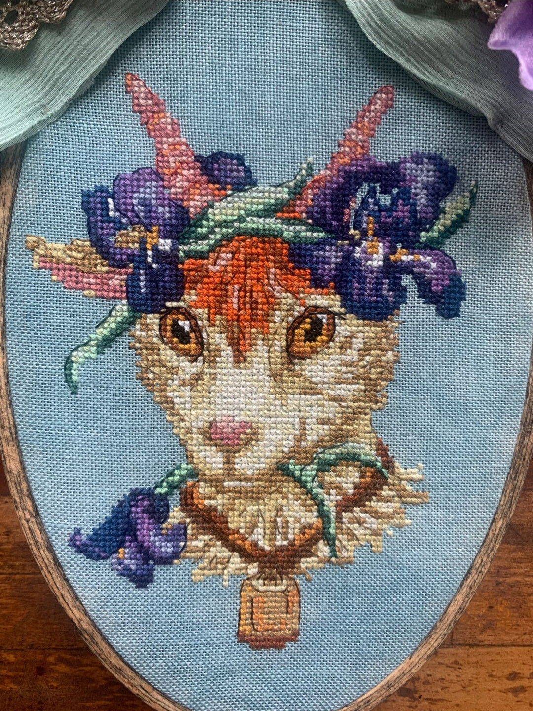 Embroidery of a goat with flowers on its head in an oval frame.