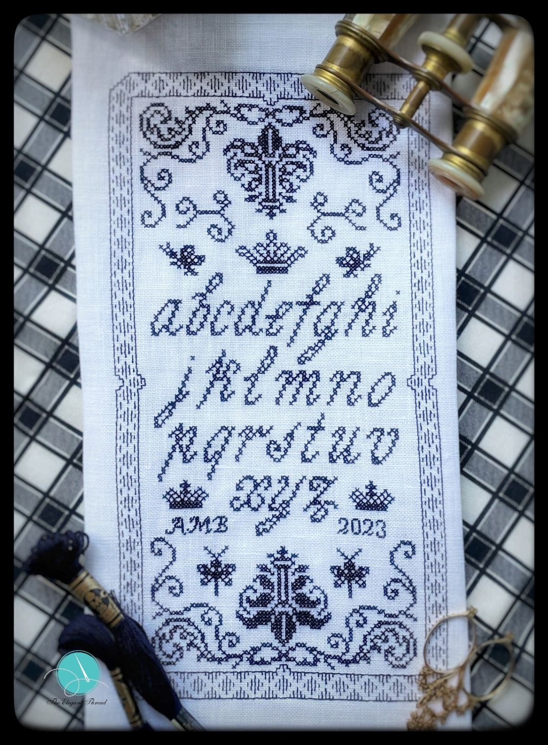 Cross-stitched alphabet pattern on fabric with decorative elements and a checkered background.