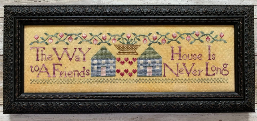 Framed cross-stitched artwork with houses and text on a wooden background