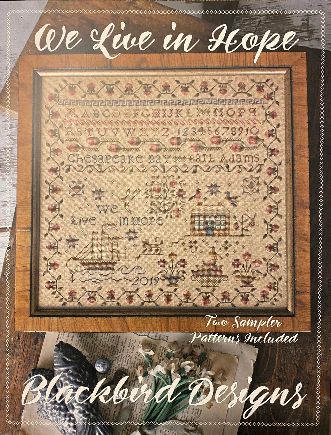 A needlecraft kit packaging for 'We Live in Hope' by Blackbird Designs featuring a needlepoint image with alphabet, numbers, a ship, and the phrases 'We Live in Hope' and 'Hope springs eternal'.