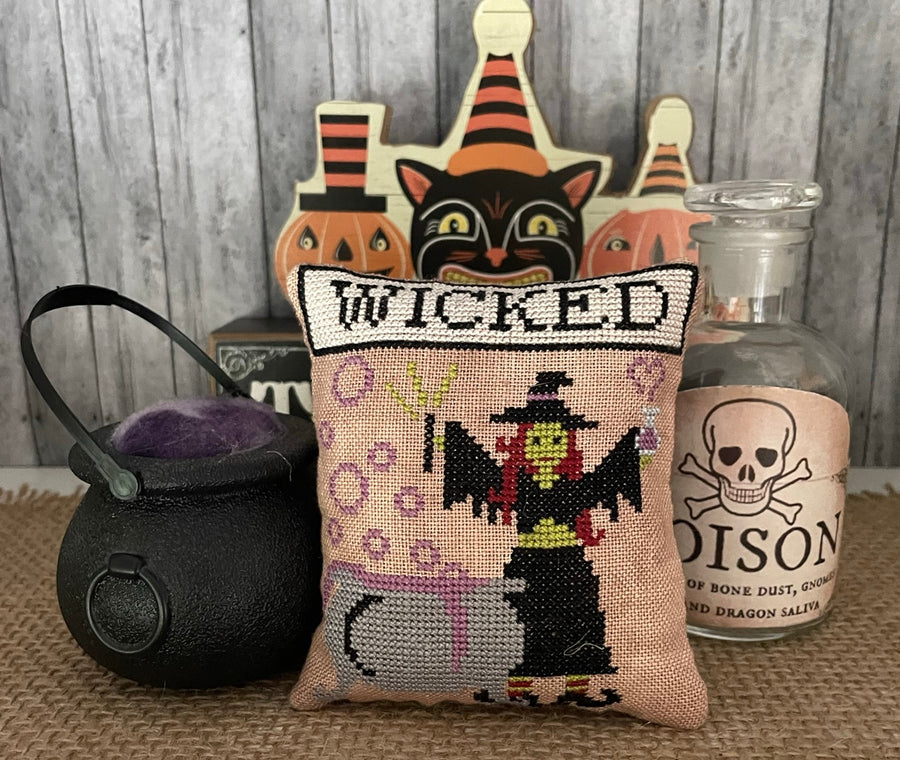 Halloween-themed pillow with witch design, cauldron, and potion bottle on a wooden surface.