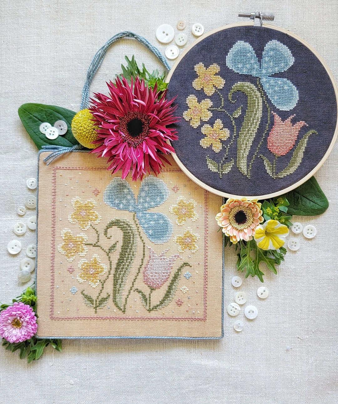 A collection of embroidered wildflower designs on fabric, accompanied by real flowers and displayed in a hoop.