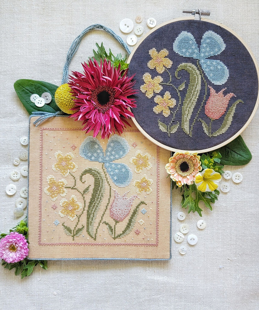 A collection of embroidered wildflower designs on fabric, accompanied by real flowers and displayed in a hoop.