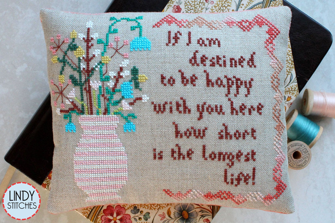 Cross-stitched pillow with a quote and floral design, featuring Lindy Stitches branding.